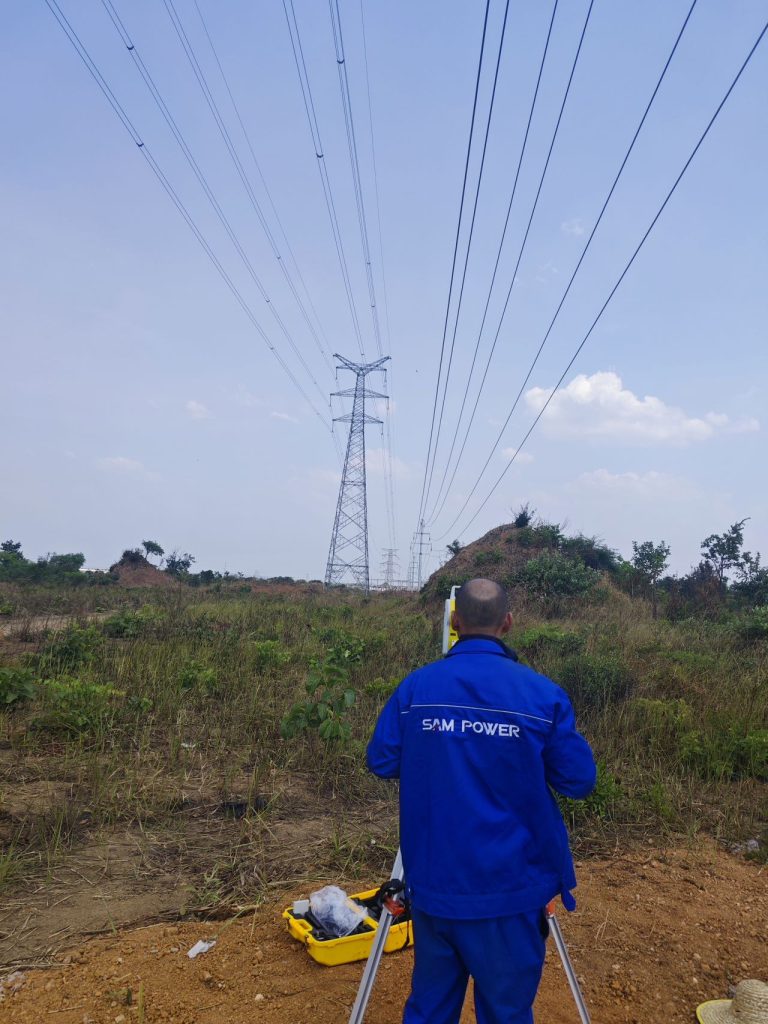 Un employé de Sam Power portant un uniforme bleu, en train d'installer un poteau électrique